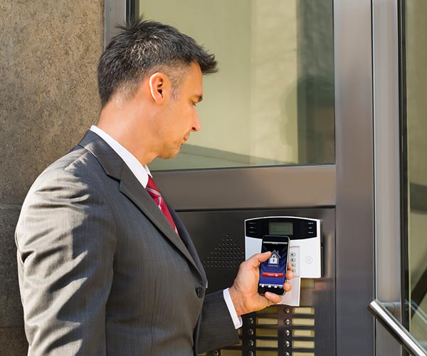 a man accessing a building with a phone on a keypad that recently received Access Control Installation in Arvada, Front Range, CO, Cheyenne, Denver, Littleton, Boulder